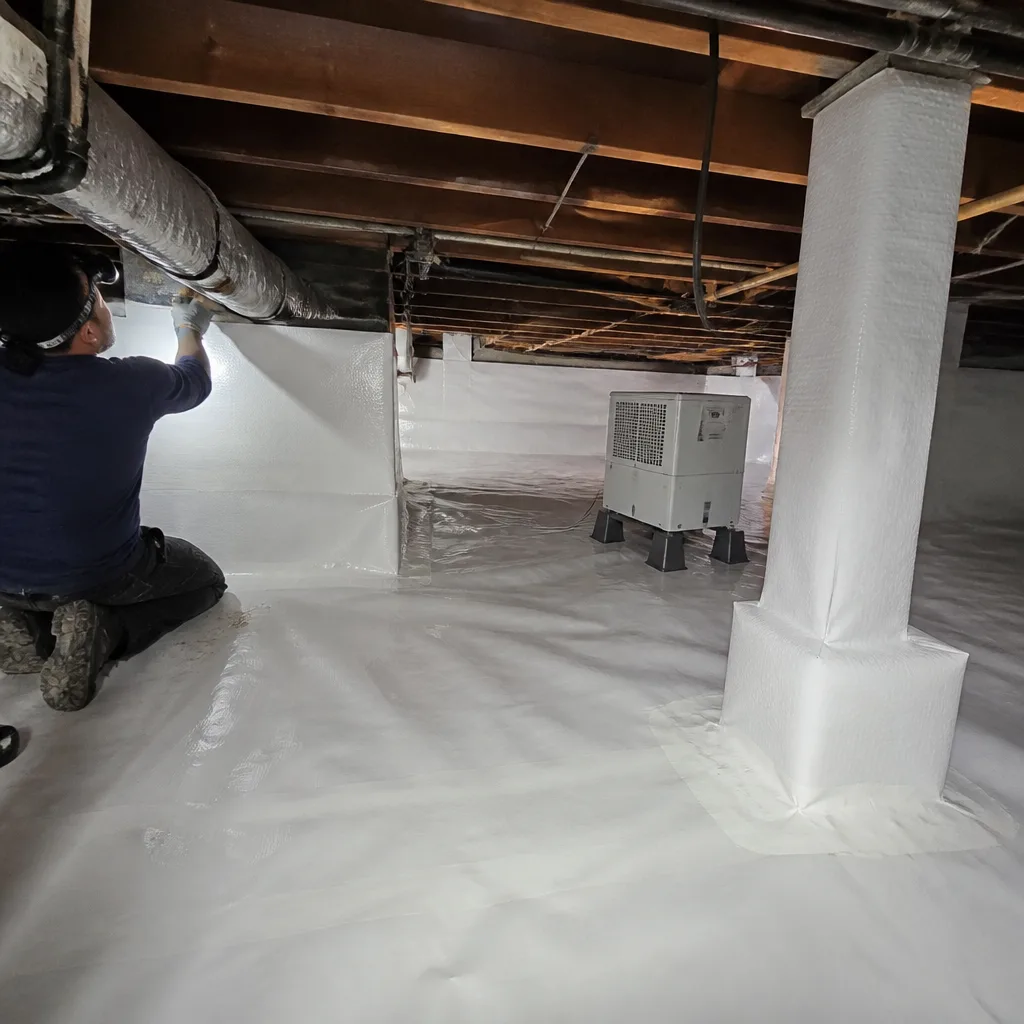 Technician performing professional crawl space encapsulation with a white vapor barrier.